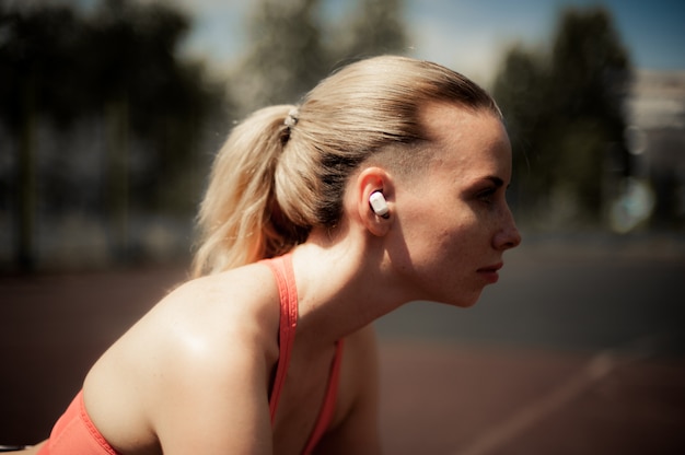Fitness mulher ouvindo música em fones de ouvido sem fio, fazendo exercícios de treino na rua