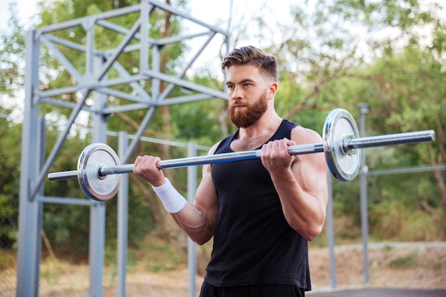 Fitness musculoso barbudo treino de homem bonito com barra ao ar livre