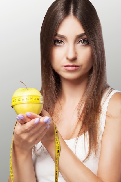 Fitness Una niña se adhiere a una dieta y sostiene una manzana con una cinta métrica