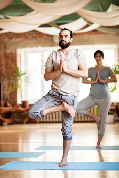 fitness, pessoas e conceito de estilo de vida saudável - homem e mulher fazendo ioga em pose de árvore no estúdio