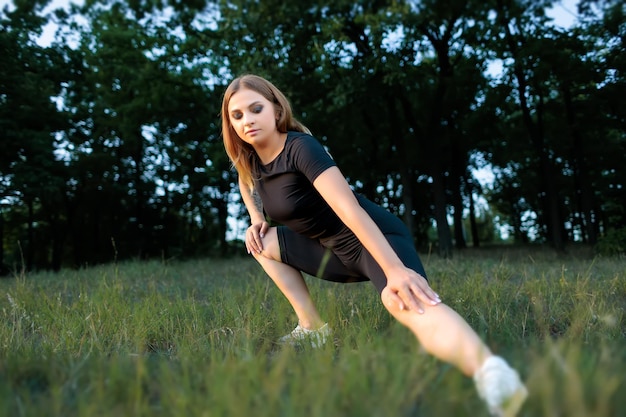 Fitness rubia va a hacer deporte en el parque haciendo estiramientos de piernas