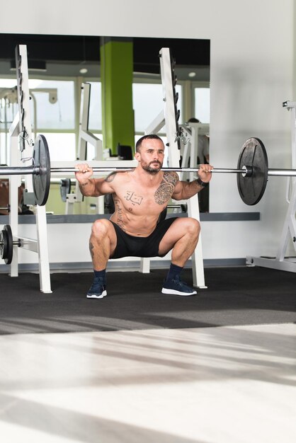 Fitness saludable hombre trabajando las piernas con pesas en un ejercicio en cuclillas de gimnasio