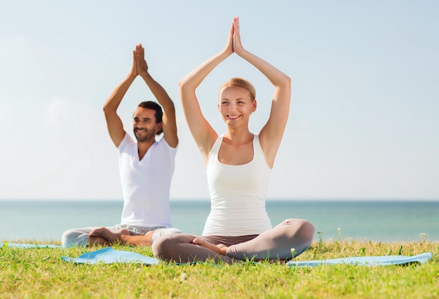 Fitness-, Sport-, Freundschafts- und Lifestyle-Konzept - lächelndes Paar, das Yoga-Übungen auf Matten im Freien macht