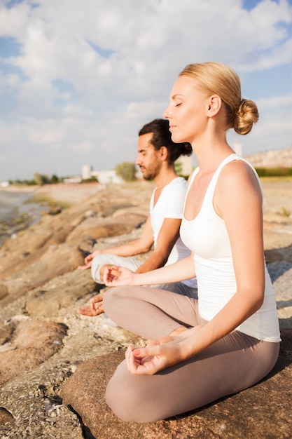 Fitness-, Sport-, Freundschafts- und Lifestyle-Konzept - lächelndes Paar, das Yoga-Übungen im Freien macht