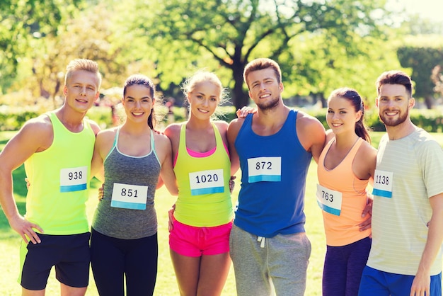 Foto fitness, sport, marathon, freundschaft und gesundes lebensstilkonzept - gruppe glücklicher jugendlicher freunde oder sportlerpaare mit rennabzeichennummern im freien