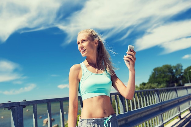 Fitness-, Sport-, Menschen-, Technologie- und gesundes Lebensstilkonzept - lächelnde junge Frau mit Smartphone, die im Freien trainiert