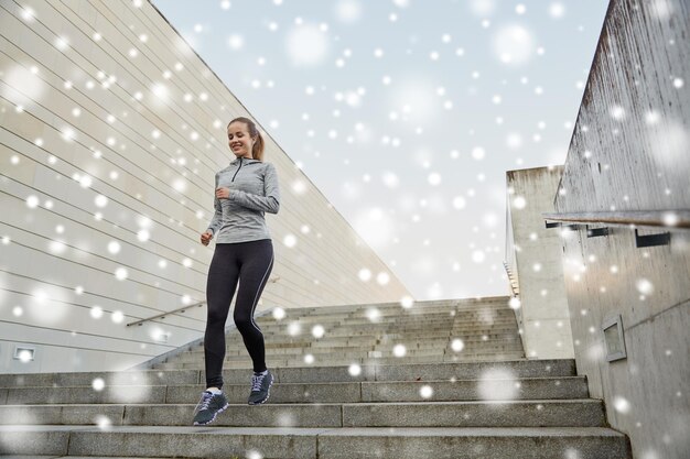 Fitness, Sport, Menschen und gesunder Lebensstil Konzept - glückliche sportliche Frau, die in der Stadt die Treppe runterläuft