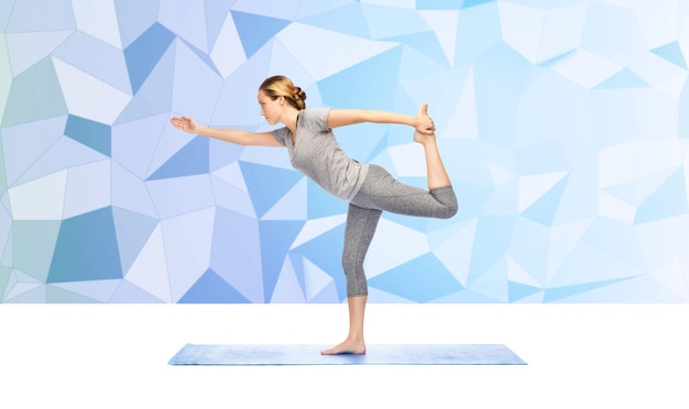 Fitness, Sport, Menschen und gesundes Lifestyle-Konzept - Frau, die Yoga in Lord of the Dance-Pose auf Matte über blauem polygonalem Hintergrund macht