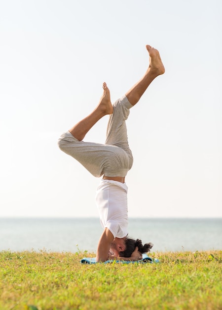 Fitness-, Sport-, People- und Lifestyle-Konzept - Mann macht Yoga-Übungen auf Sand im Freien