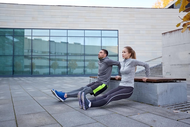 Fitness, Sport, Training, Menschen und Lifestyle-Konzept - Paar macht Trizeps-Dip-Übungen auf der Bank im Freien
