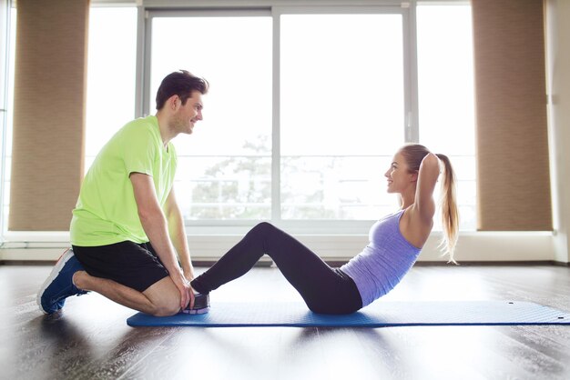 Fitness, Sport, Training, Teamwork und People-Konzept - Frau mit Personal Trainer beim Sit-ups im Fitnessstudio