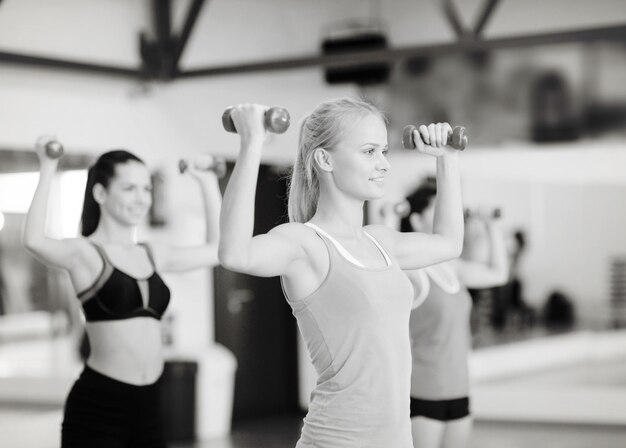 Fitness-, Sport-, Trainings-, Fitness- und Lifestyle-Konzept - Gruppe lächelnder Frauen, die im Fitnessstudio mit Hanteln trainieren