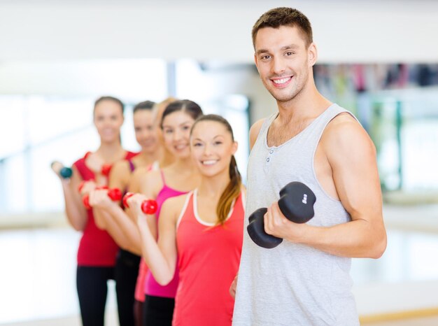 Fitness-, Sport-, Trainings-, Fitness- und Lifestyle-Konzept - Gruppe lächelnder Menschen, die Hanteln im Fitnessstudio heben