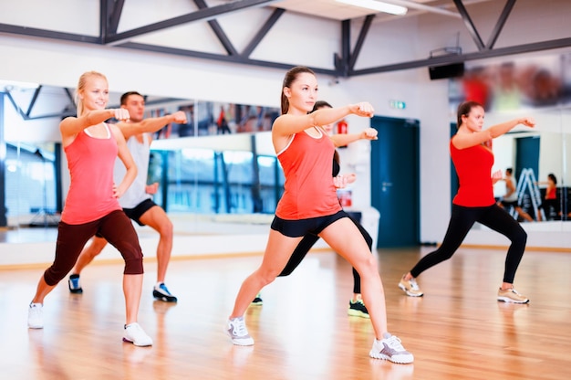 Fitness-, Sport-, Trainings-, Fitness- und Lifestyle-Konzept - Gruppe lächelnder Menschen, die im Fitnessstudio trainieren