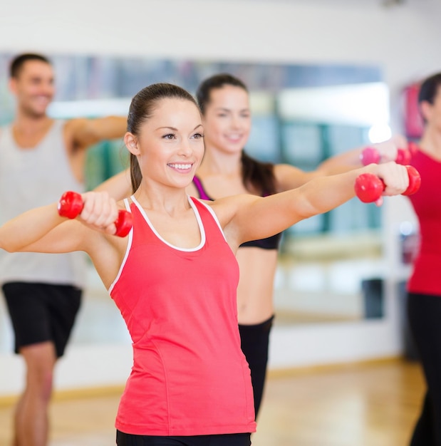 Fitness-, Sport-, Trainings-, Fitness- und Lifestyle-Konzept - Gruppe lächelnder Menschen, die mit Hanteln im Fitnessstudio trainieren