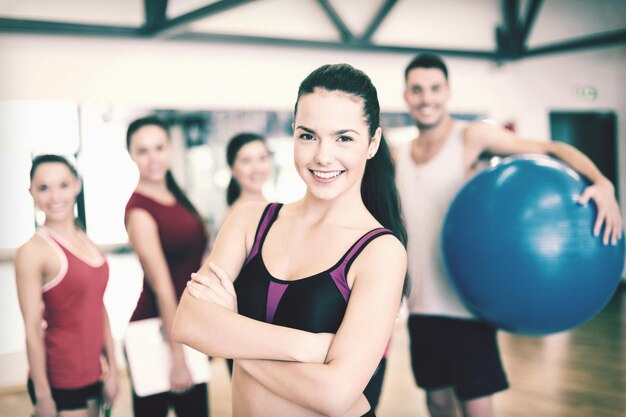 Fitness-, Sport-, Trainings-, Fitness- und Lifestyle-Konzept - lächelnde Frau, die vor der Gruppe von Menschen im Fitnessstudio steht