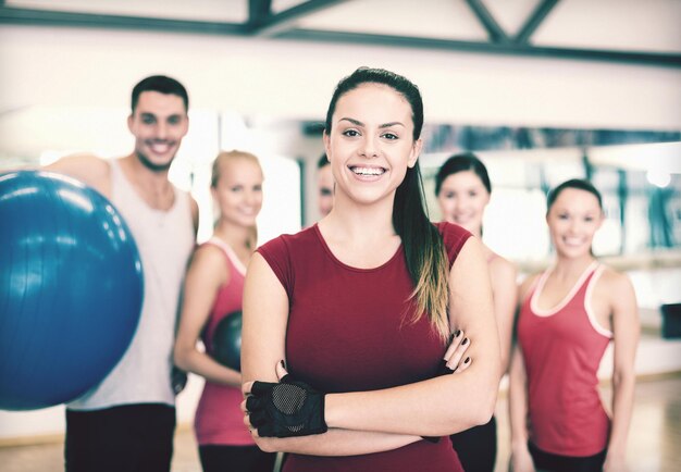 Fitness-, Sport-, Trainings-, Fitness- und Lifestyle-Konzept - lächelnde Frau, die vor der Gruppe von Menschen im Fitnessstudio steht
