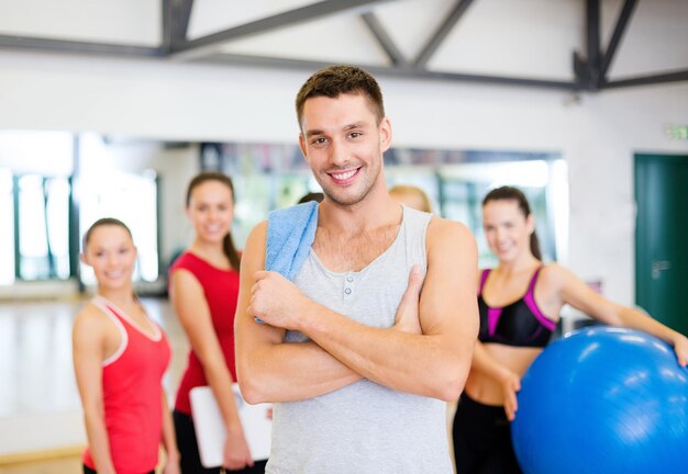 Fitness-, Sport-, Trainings-, Fitness- und Lifestyle-Konzept - lächelnder Mann, der vor der Gruppe von Menschen im Fitnessstudio steht