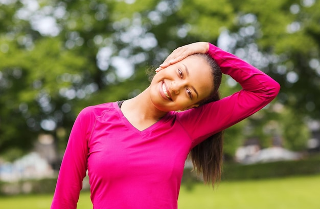 Fitness-, Sport-, Trainings-, Park- und Lifestyle-Konzept - lächelnde Frau, die sich im Freien das Bein streckt