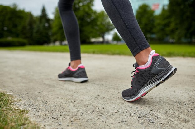 Fitness-, Sport-, Trainings-, People- und Lifestyle-Konzept - Nahaufnahme von Frauenfüßen, die von hinten auf der Strecke laufen