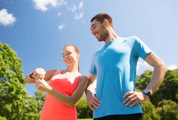 Fitness-, Sport-, Trainings-, Technologie- und Lifestyle-Konzept - zwei lächelnde Menschen mit Herzfrequenzuhren im Freien