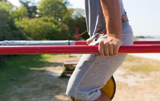 Fitness-, Sport-, Trainings-, Trainings- und Lifestyle-Konzept - Nahaufnahme eines jungen Mannes, der Trizeps-Dip mit Gewichtsgürtel auf Barren im Freien macht