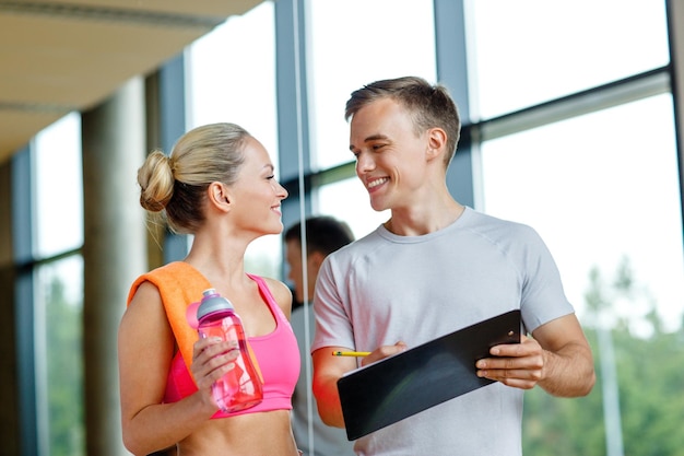 Fitness-, Sport-, Trainings- und Ernährungskonzept - lächelnde junge Frau mit Personal Trainer nach dem Training im Fitnessstudio