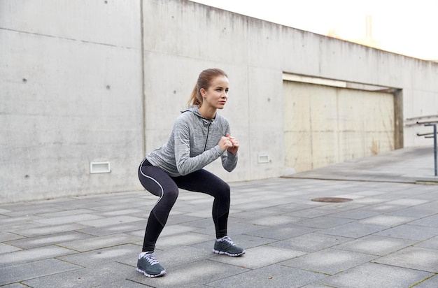 Fitness-, Sport-, Trainings- und gesundes Lifestyle-Konzept - glückliche Frau, die im Freien Kniebeugen macht