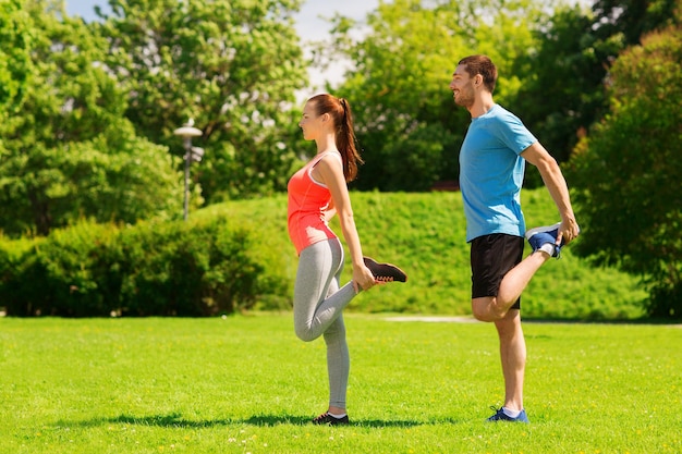 Fitness-, Sport-, Trainings- und Lifestyle-Konzept - lächelndes Paar, das sich im Freien ausdehnt