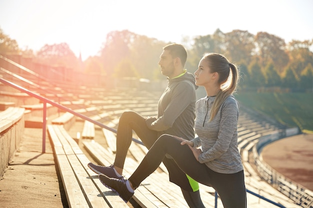 Fitness-, Sport-, Trainings- und Lifestyle-Konzept - Paar streckt Bein auf Tribünen des Stadions