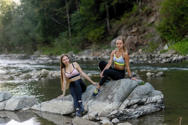 Fitness-, Sport-, Yoga- und gesundes Lifestyle-Konzept - Glückliche Freundinnen, die nach dem Training auf den Wiesen sitzen. Fitness-Frauen sitzen zusammen und entspannen sich nach dem Training.