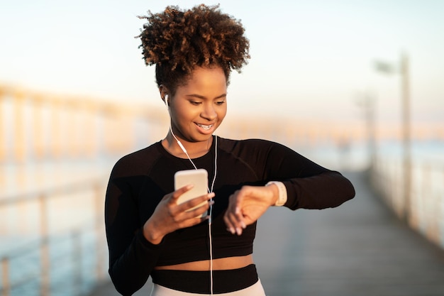 Fitness tracker deportivo mujer negra mirando smartwatch después de entrenar al aire libre