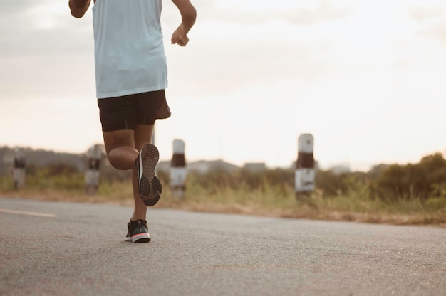 Fitness, treino, corrida, exercício, estilo de vida e conceito saudável. O homem está correndo para se exercitar para sua saúde à beira da estrada ao pôr do sol.