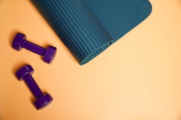 Fitness-Zubehörkonzept Lila Hantel Sport mit blauer Yoga-Matte auf orangefarbenem Hintergrund Kopierraum Flachlag Sicht von oben