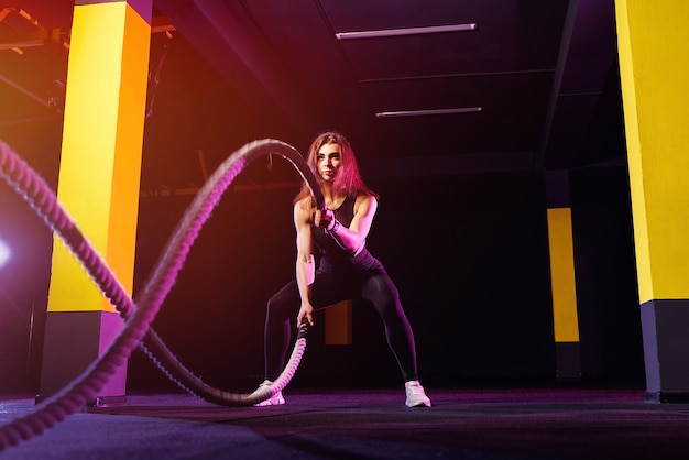 Fitnessfrau, die trainingsseile für übung im fitnessstudio verwendet. athlet, der mit kampfseilen im cross-gym trainiert.