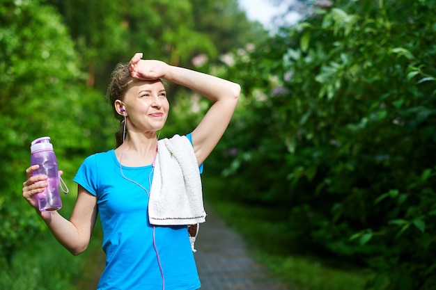 Fitnessfrau mit Flasche und Handtuch Wasser nach dem Lauftraining im Sommerpark