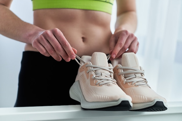 Fitnessfrau mit schmaler Passform, die Sportbekleidung trägt, hält beige Turnschuhe zum Joggen und Laufen. Sport treiben und fit sein. Sportler mit gesundem sportlichem Lebensstil