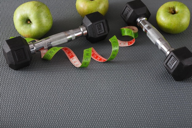 Fitnessgeräte. Gesunder Lebensstilhintergrund mit Kopienraum auf Grau. Hanteln, Apfel und Maßband