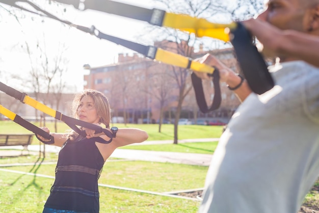 Fitnesspaar, das mit Trx-Fitnessgurten im Park trainiert. Erwachsener Mann und Frau, die draußen trainieren.