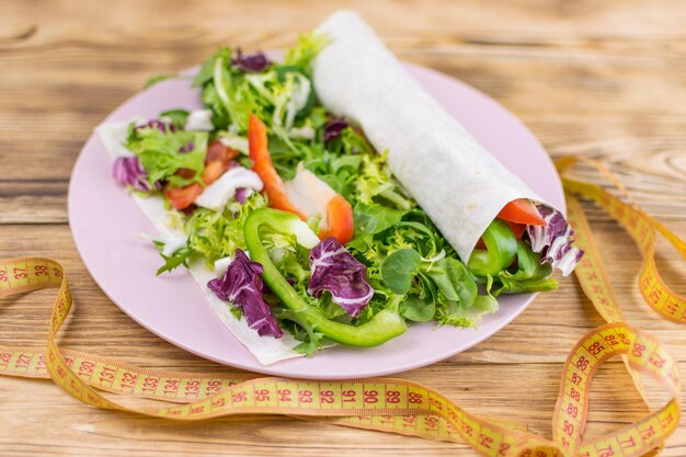 Fitnesssalat und Maßband auf rustikalem Holztisch Gemischte grüne Tomaten, Olivenöl und Gewürze für ein gesundes Lebensstilkonzept