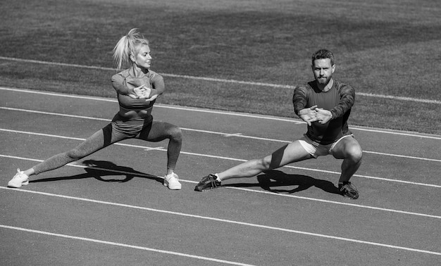 Fitnesssportler und -frau wärmen sich auf und dehnen sich gemeinsam auf der Rennstrecke des Stadions im Freien mit Sportbekleidungstrainer