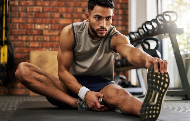 Fitnessstudio-Mann sitzt und streckt Beine für das Training, Aufwärmmotivation und Fitness-Denkweise mit Hand-auf-Fuß-Fokus-Engagement und männlicher Athlet auf dem Boden, Beindehnung im Sportverein für Trainingsziele