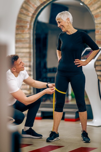 Fitnesstrainer, der das Bein einer älteren Frau misst, bevor er im Fitnessstudio trainiert.