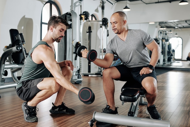 Fitnesstrainer zeigt dem Klienten, wie er den Arm strecken kann, wenn er an Bizepsmuskeln arbeitet