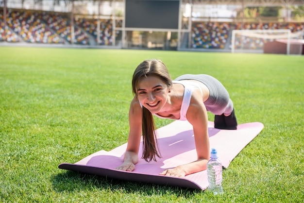 Fitnessübungen im Freien. Frau, die Morgenübungen auf Matte auf grünem Gras tut