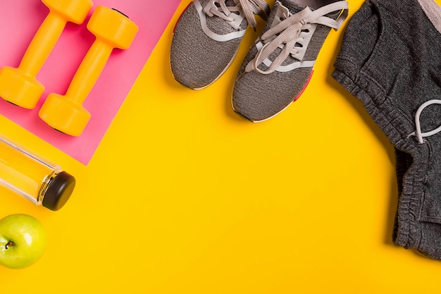 Fitnesszubehör auf gelbem Hintergrund Turnschuhe Flasche Wasser und Hanteln