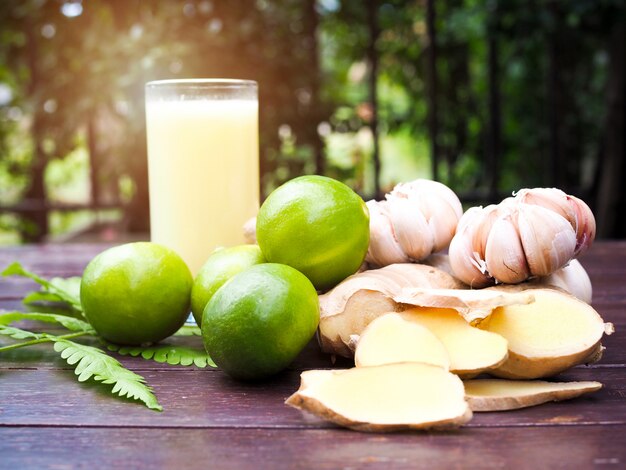 Fitoterapia com limão limão, gengibre, alho e copo de suco extraído de ervas na mesa de madeira.