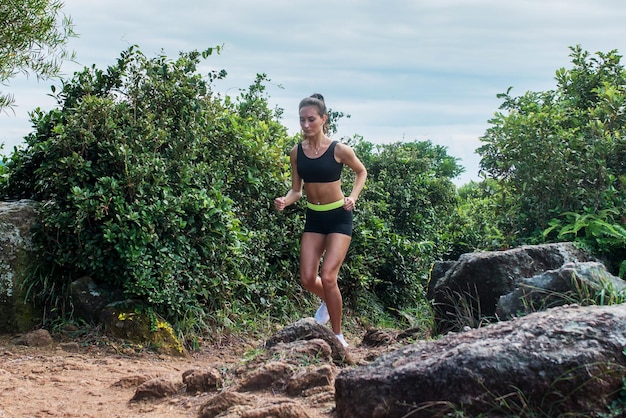 Fitte athletische junge Frau, die im Sommer auf schmutzigen felsigen Pfaden in den Bergen läuft