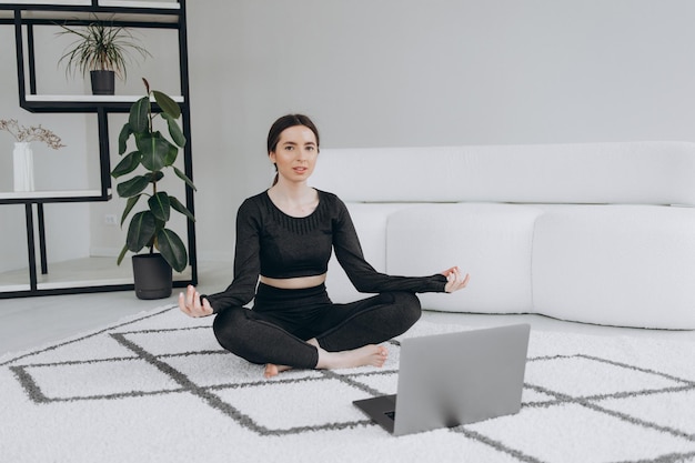 Fitte Frau, die Yoga macht und Online-Tutorials zum Laptop-Training im Wohnzimmer anschaut