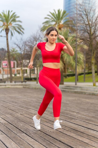 Fitte Frau in roter Kleidung, die in einem Park mit Palmen im Fitnesssport der Stadt läuft